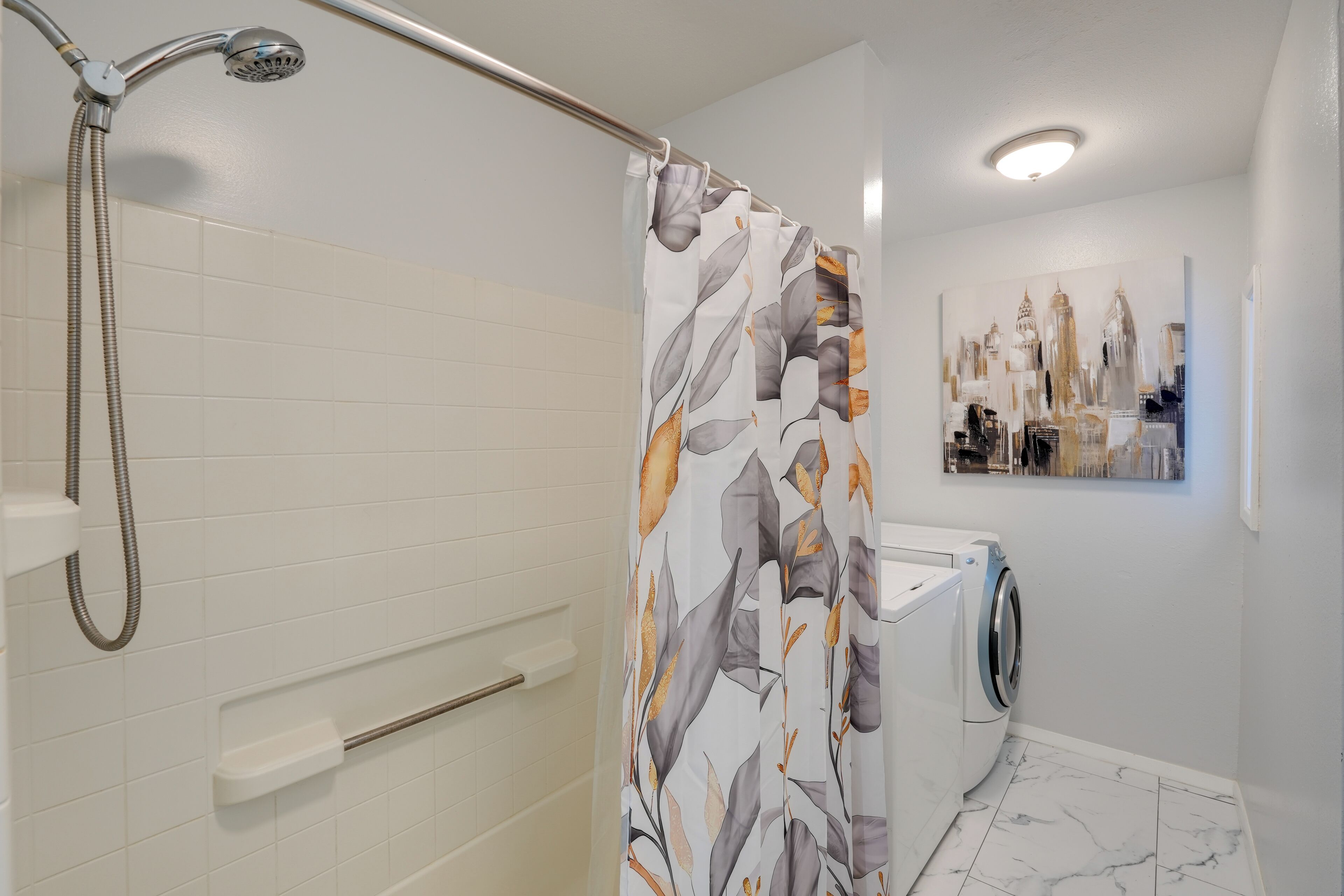 Een badkamer met een douche, toilet, wastafel en een wasmachine, plus een kunstwerk aan de muur.