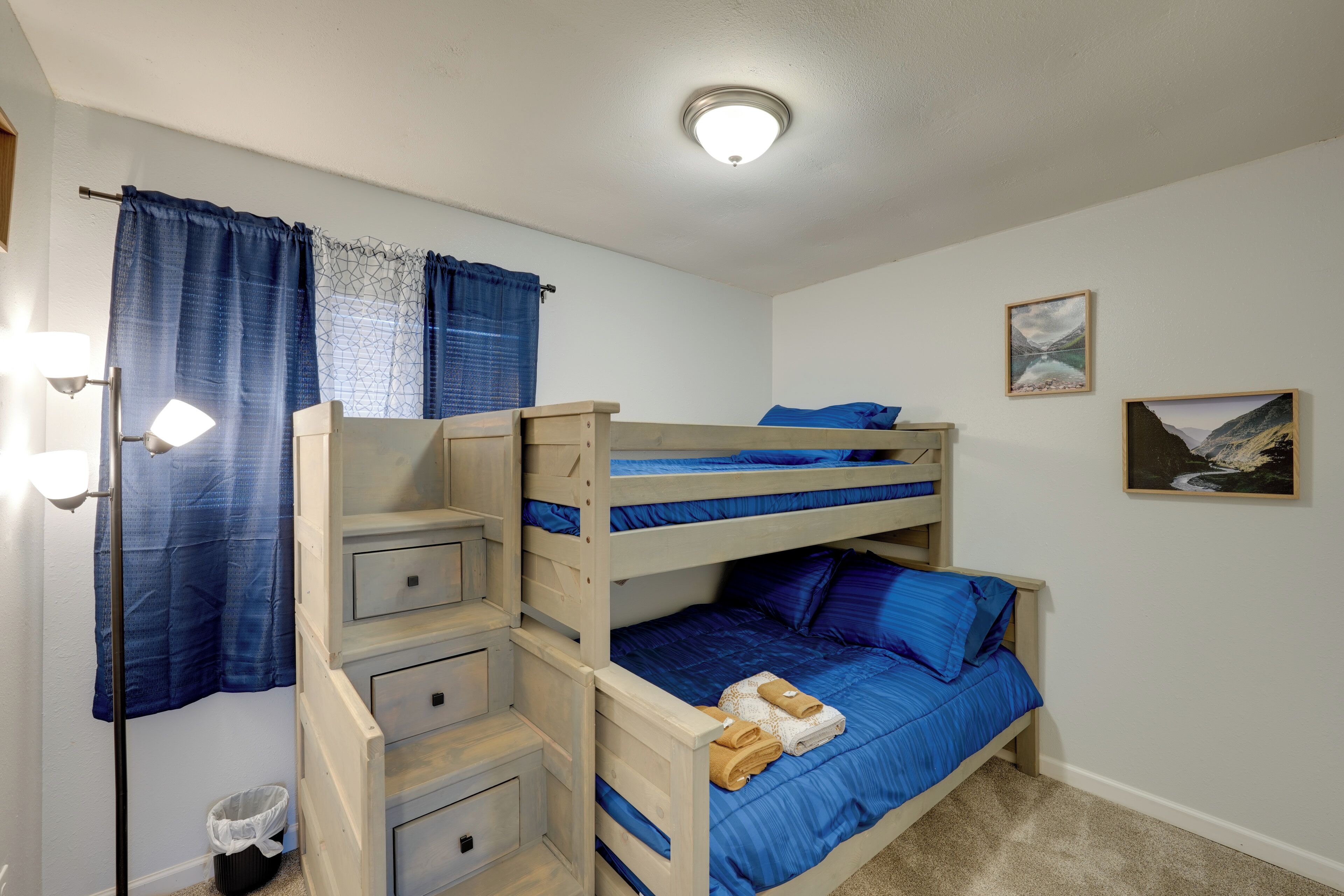 A bunk bed room with a ceiling light, a small trash bin, and two framed pictures on the wall.