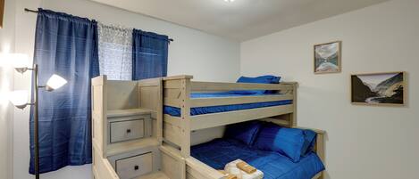 A bunk bed room with a ceiling light, a small trash bin, and two framed pictures on the wall.