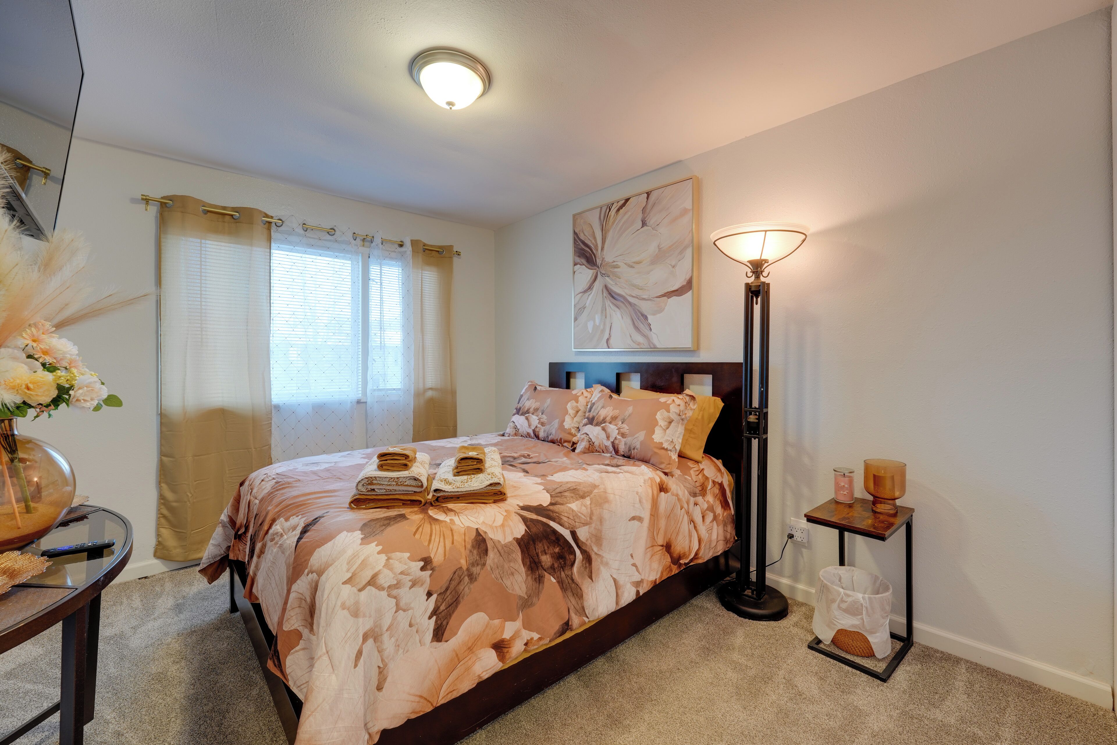 Een slaapkamer met een bed, een nachtkastje, een vloerlamp en een kunstwerk aan de muur.