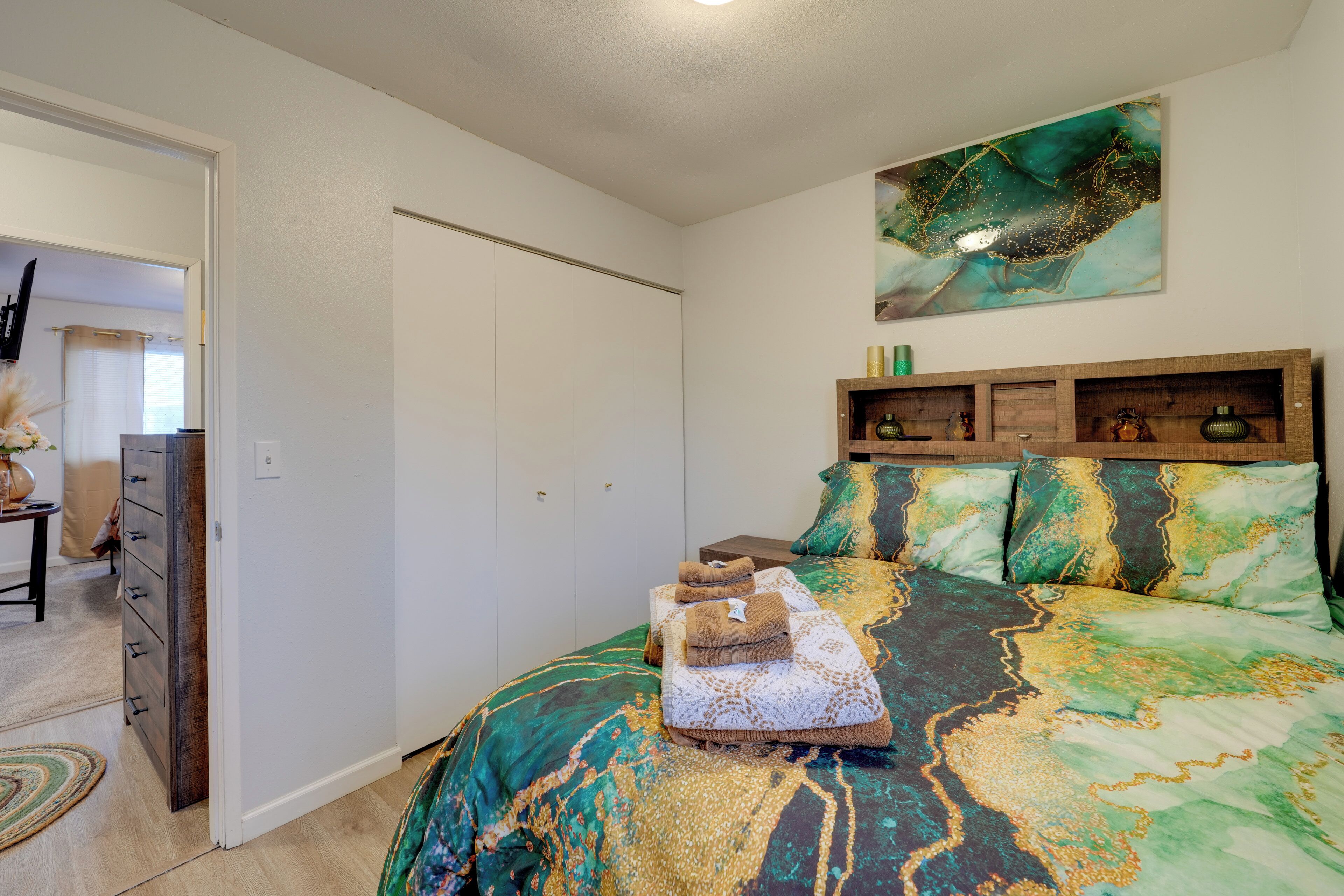 A bedroom with a bed, a wardrobe, a painting, and a small table with a vase.