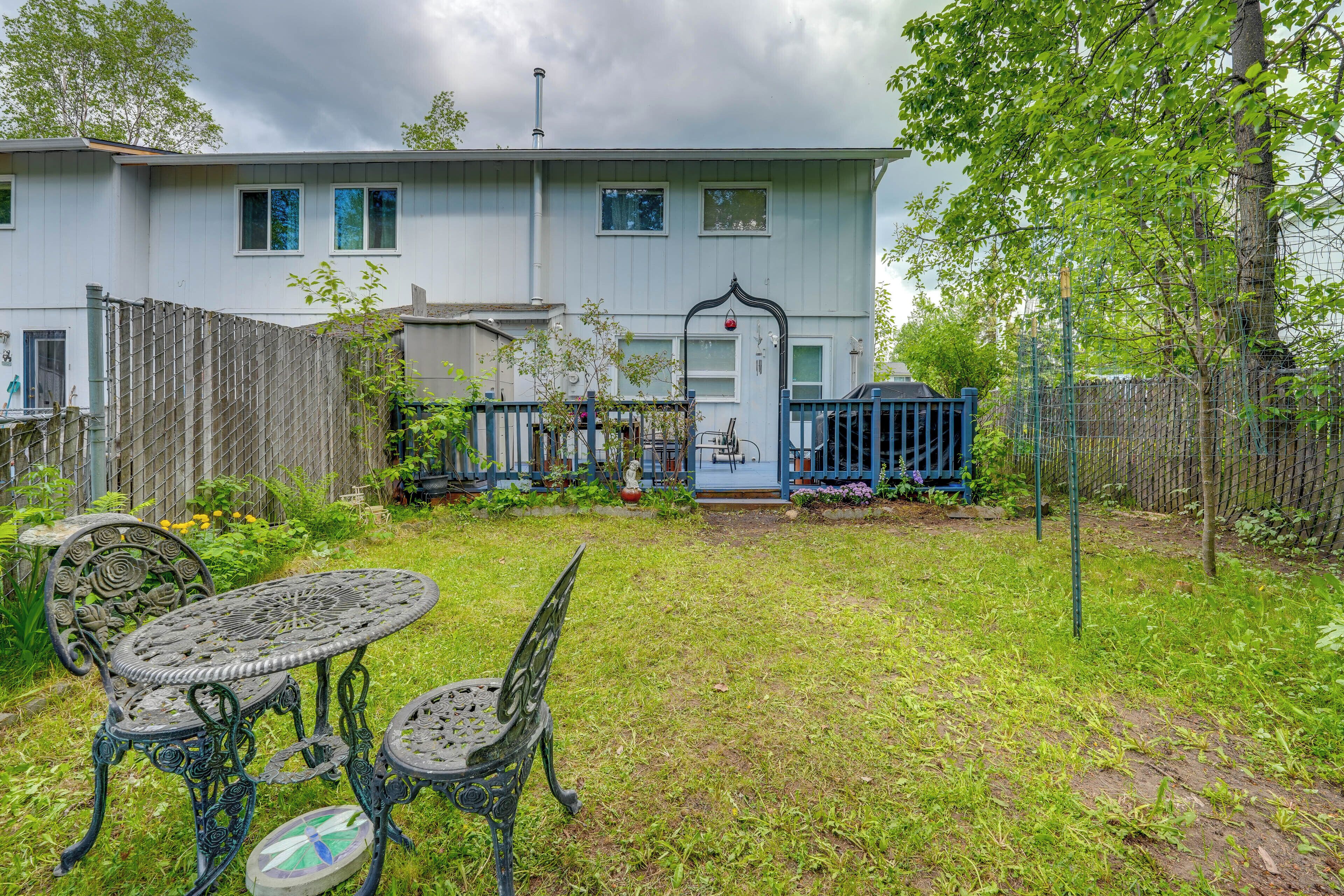 A two-story house with a fenced yard, a patio with a table and chairs, and a small garden area.