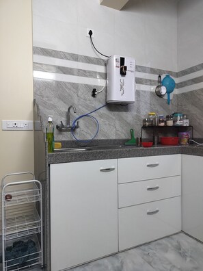 Una cocina con salpicadero de mármol, calentador de agua, un lavabo con grifo y una rejilla metálica con una cesta.