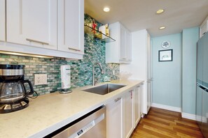 Una cocina moderna con armarios blancos, salpicadero de azulejos, pileta de acero inoxidable y lavavajillas.