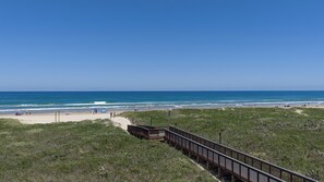 Ein Strand mit einer Holzpromenade, die zum Ufer führt, grasbewachsenen Dünen und dem Meer.