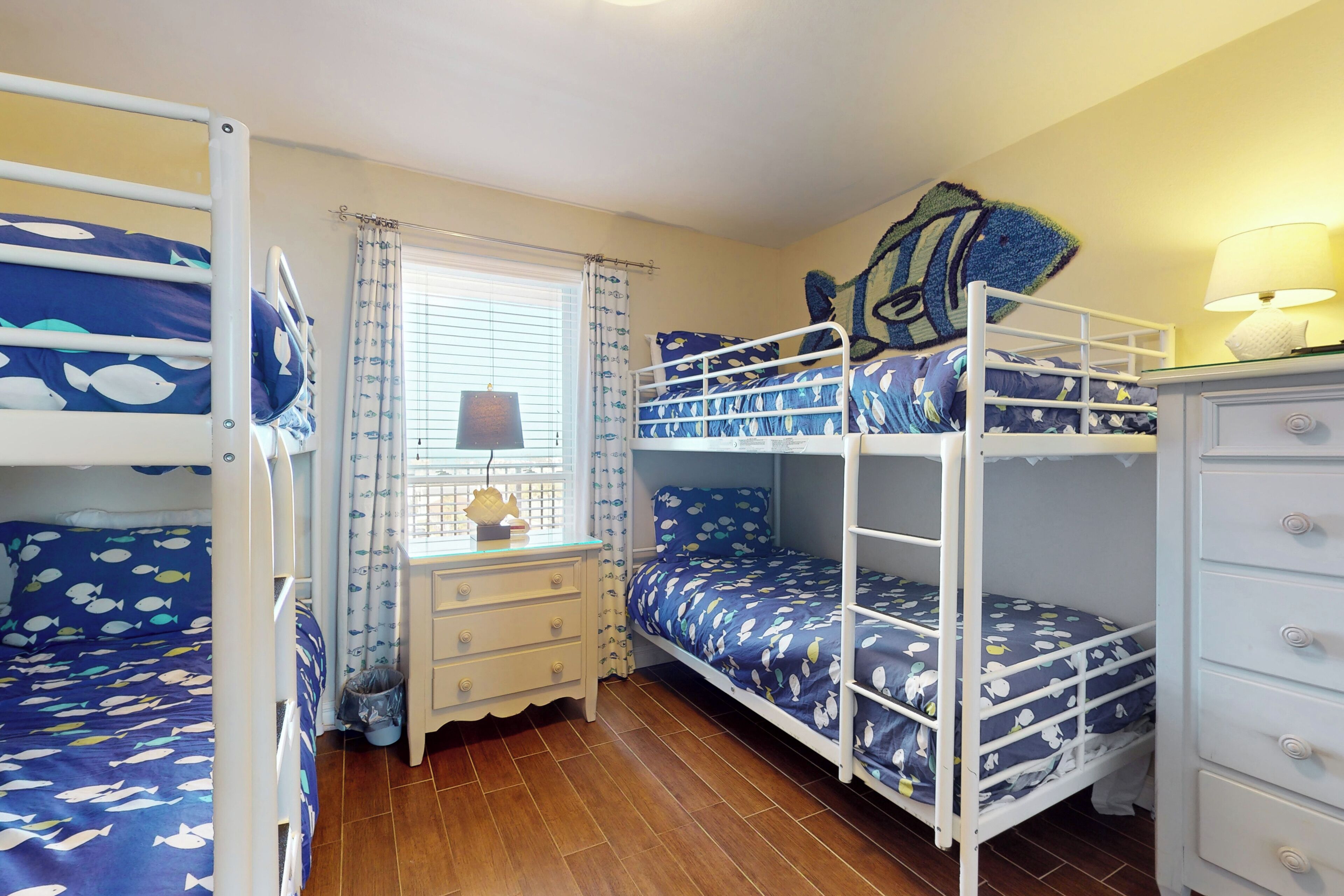 A bunk bed room with a window, curtains, a desk, and a lamp.