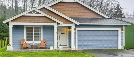 A two-story house with a garage, a front porch with wooden chairs, and a small garden area.