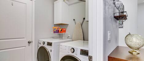 A laundry room with two front-loading washing machines, a drying rack, and a globe on a wooden shelf.