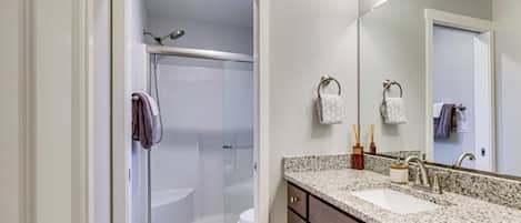 Un bagno con doccia vetrata, lavabo con piano in granito e specchio sopra il lavabo.