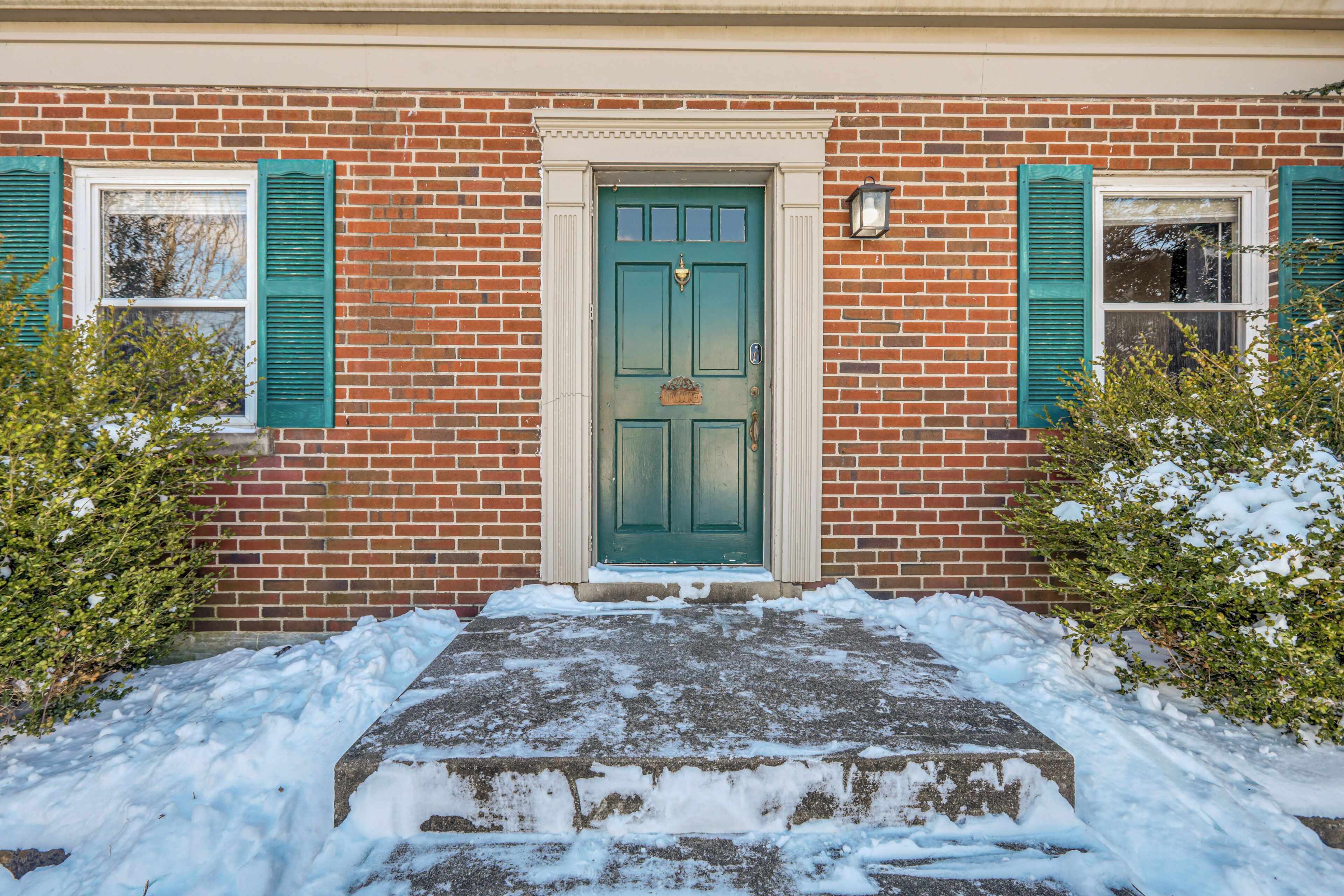 A brick building with a green door, two windows with green shutters, and a snow-covered front steps.