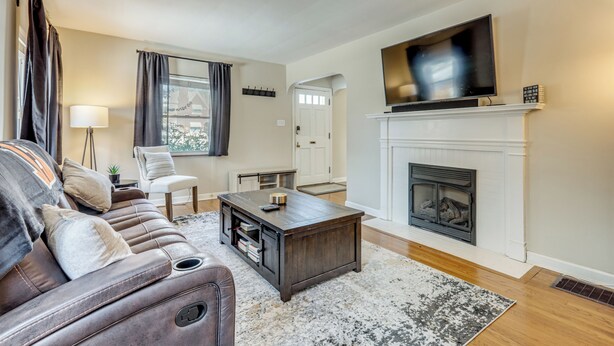 A living room with a leather sofa, a coffee table, a fireplace, and a television mounted above it.