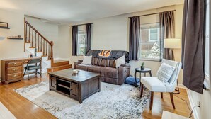 A living room with a brown leather sofa, a wooden coffee table, a white armchair, a small side table, and a staircase leading to another level.