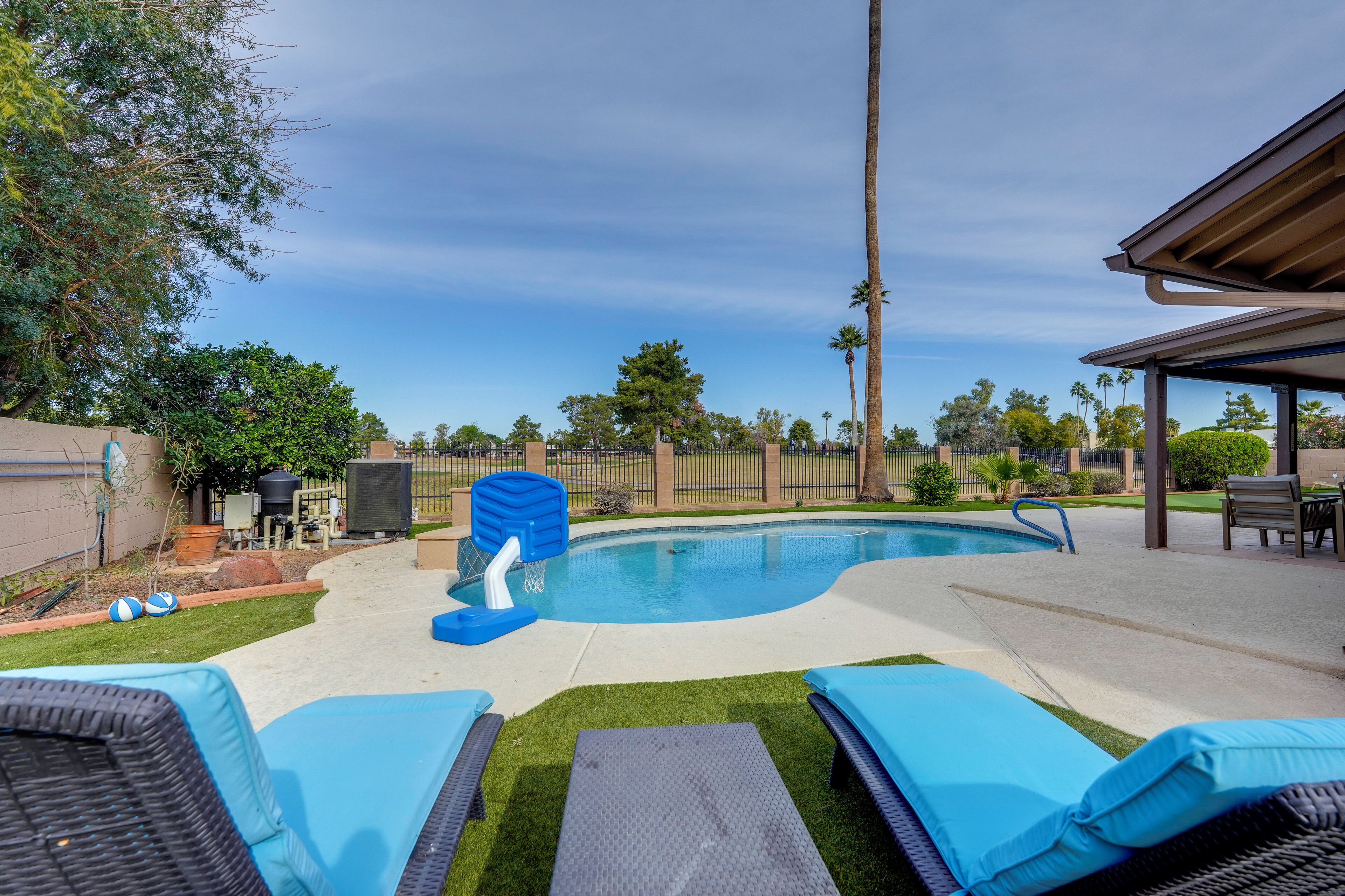 A backyard with a swimming pool, lounge chairs, and a covered patio area.