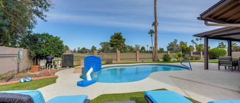 A backyard with a swimming pool, lounge chairs, and a covered patio area.