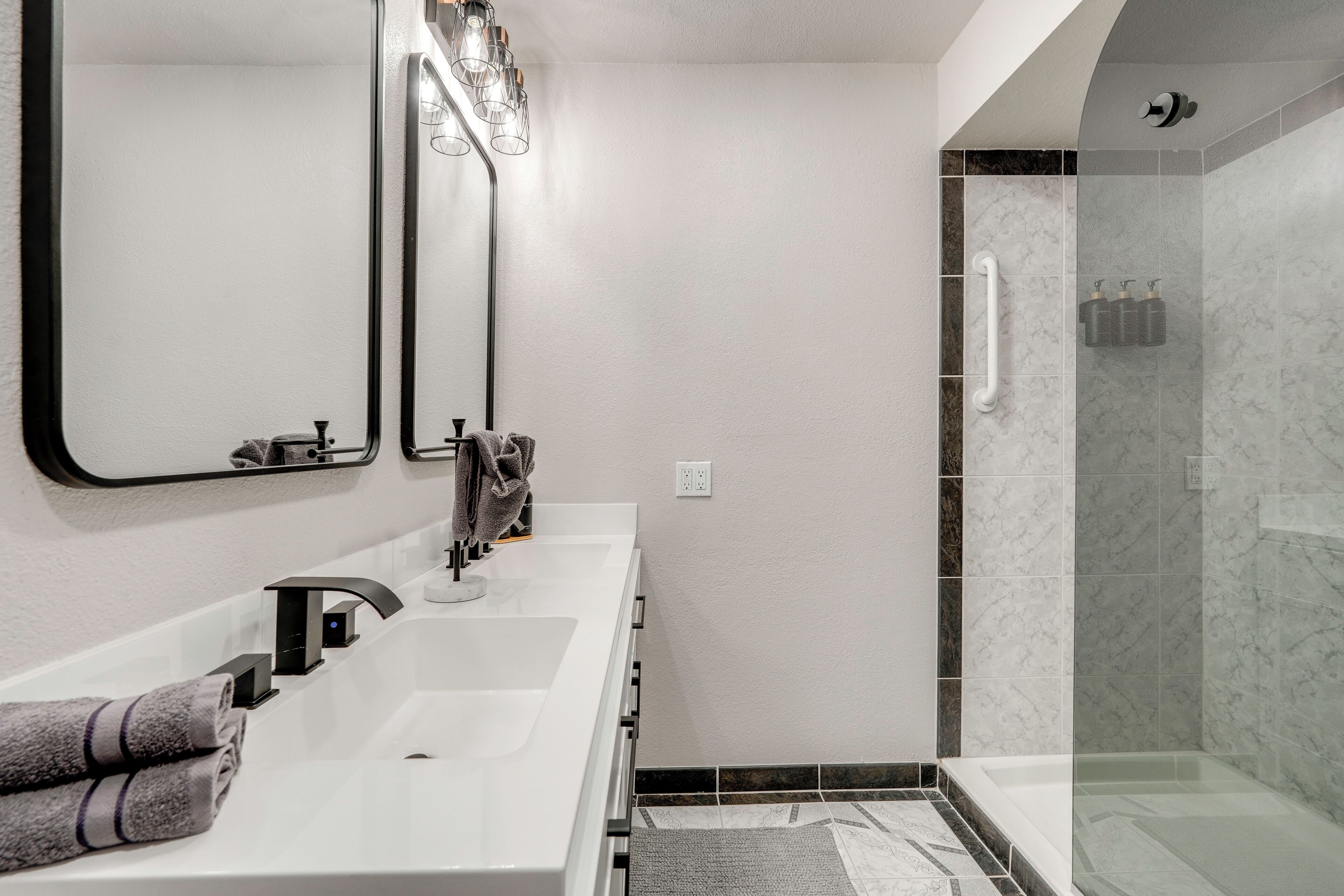 A modern bathroom with a white sink, a large mirror, and a glass-enclosed shower area.