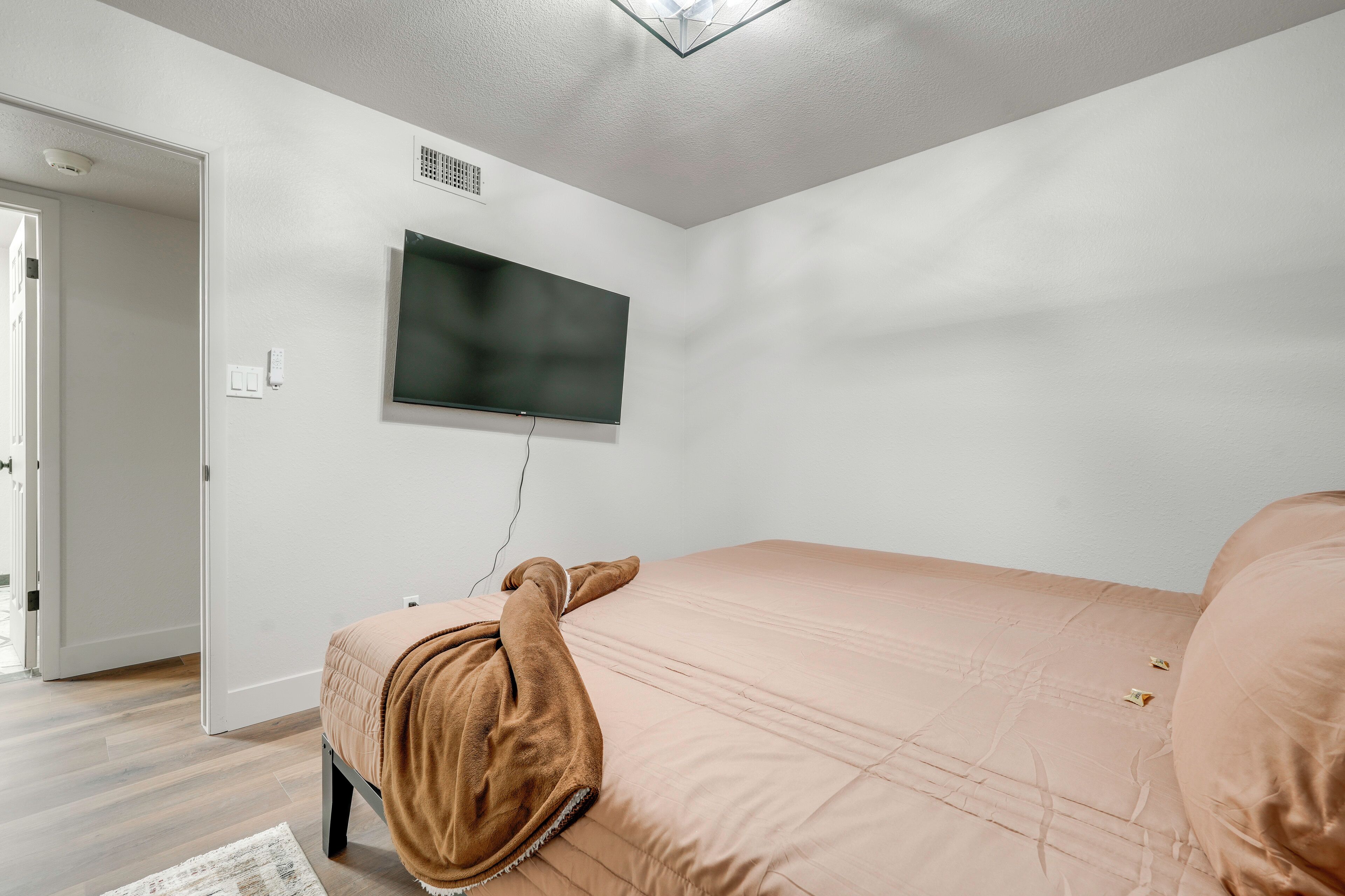 A bedroom with a bed, a television mounted on the wall, and a door leading to another room.