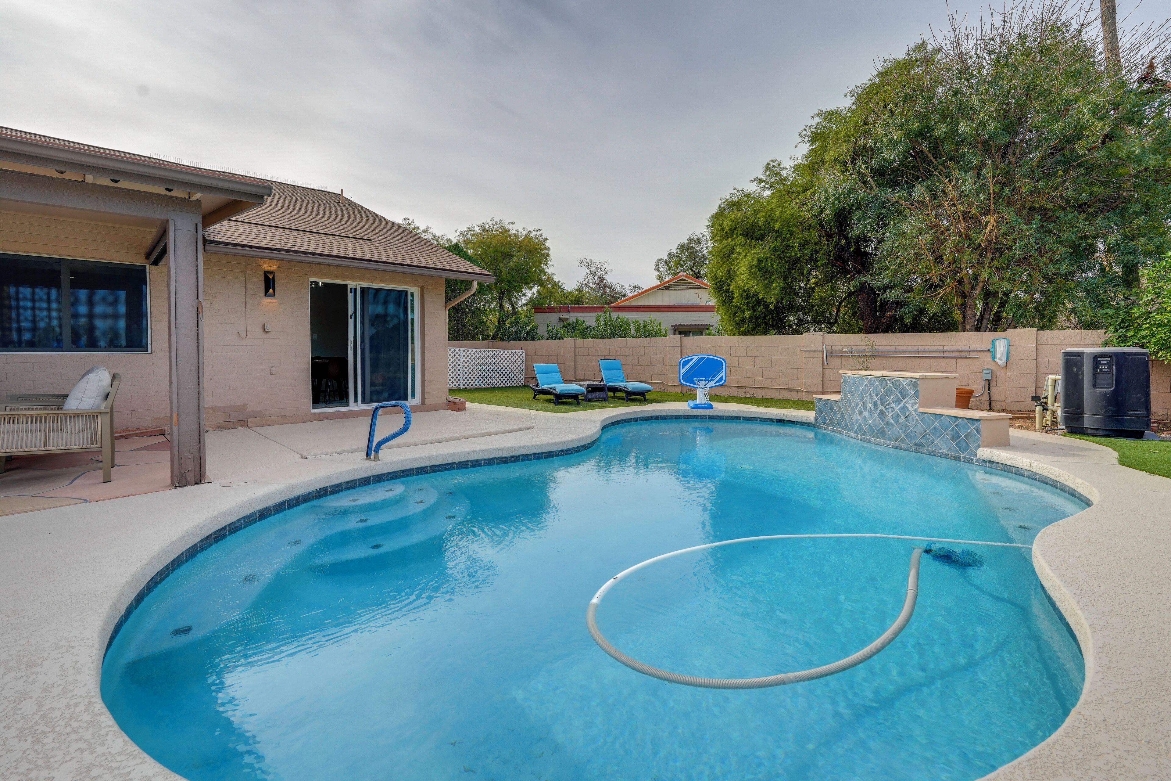 A swimming pool with a built-in hot tub, lounge chairs, and a covered patio area.