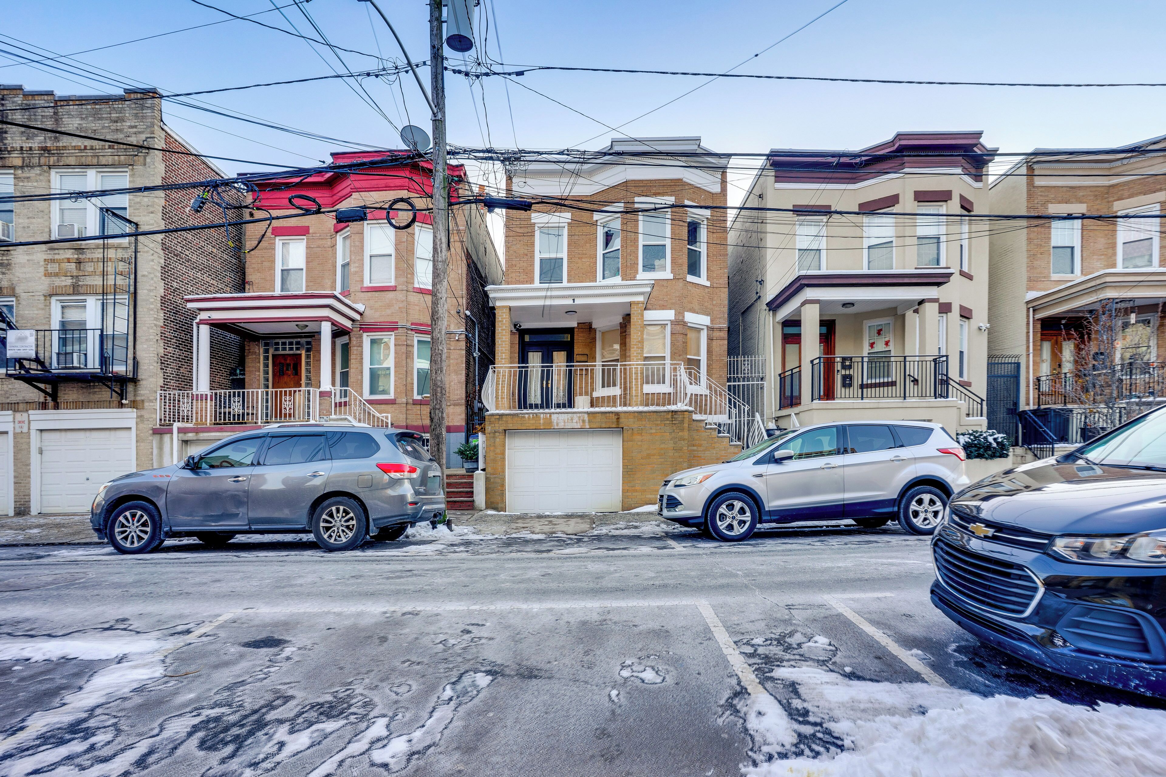 A row of townhouses with a garage, a street with parked cars, and overhead power lines.