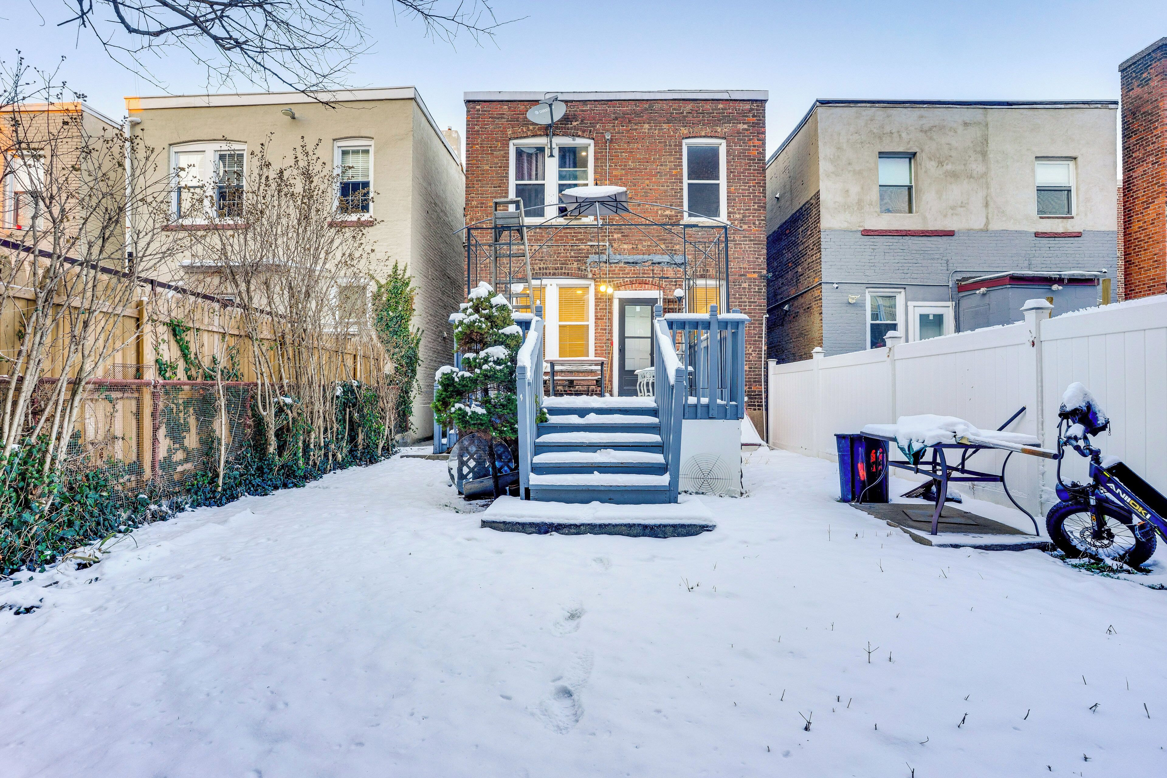 Zona residencial cubierta de nieve con una escalera que lleva a una puerta, una bicicleta y una valla.