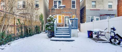 Zona residencial cubierta de nieve con una escalera que lleva a una puerta, una bicicleta y una valla.