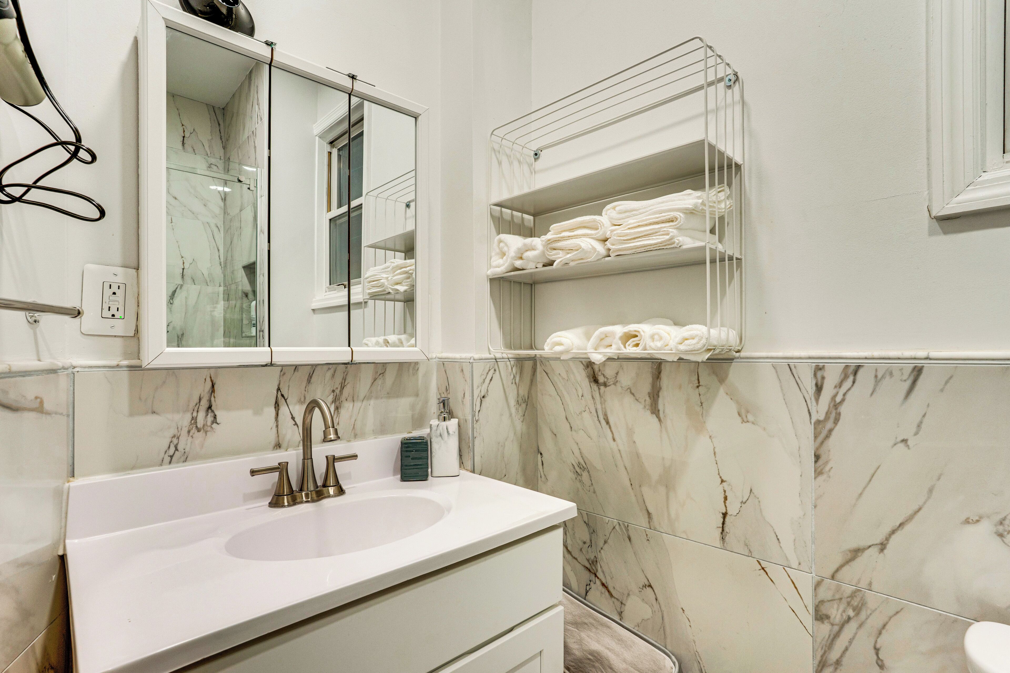 Un baño con lavamanos blanco, un espejo y un perchero para toallas.