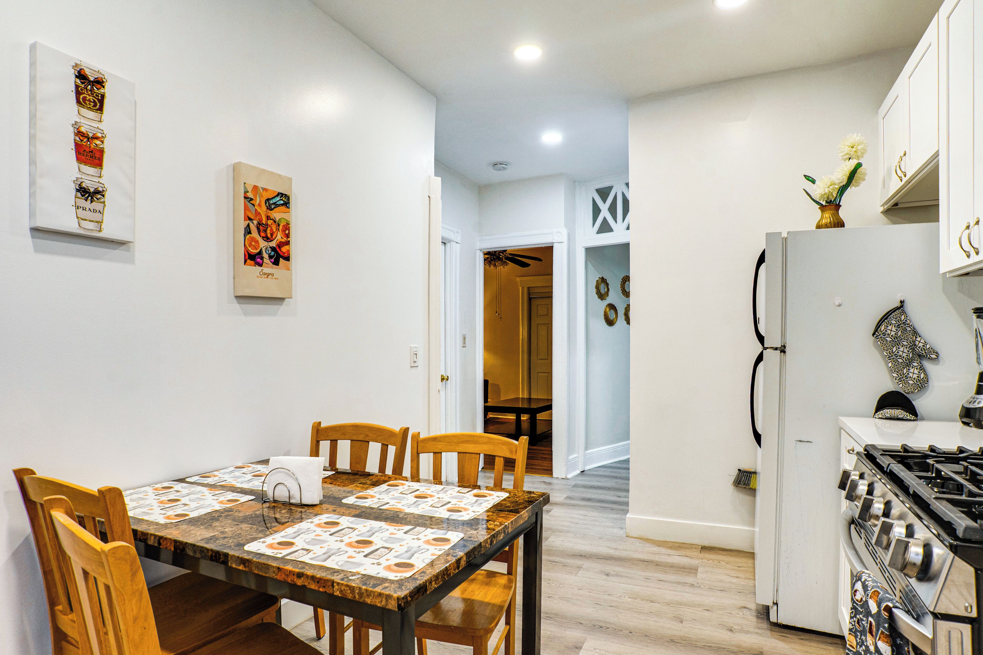 A dining area with a wooden table and chairs, a kitchen with a stove and refrigerator, and a hallway leading to another room.