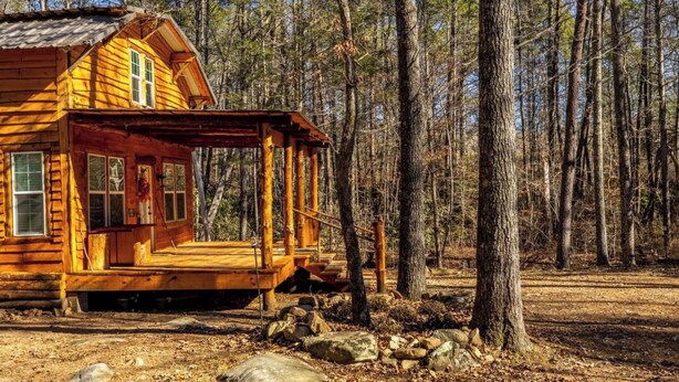 Un chalet rustique doté d’une véranda, entouré d’une forêt.