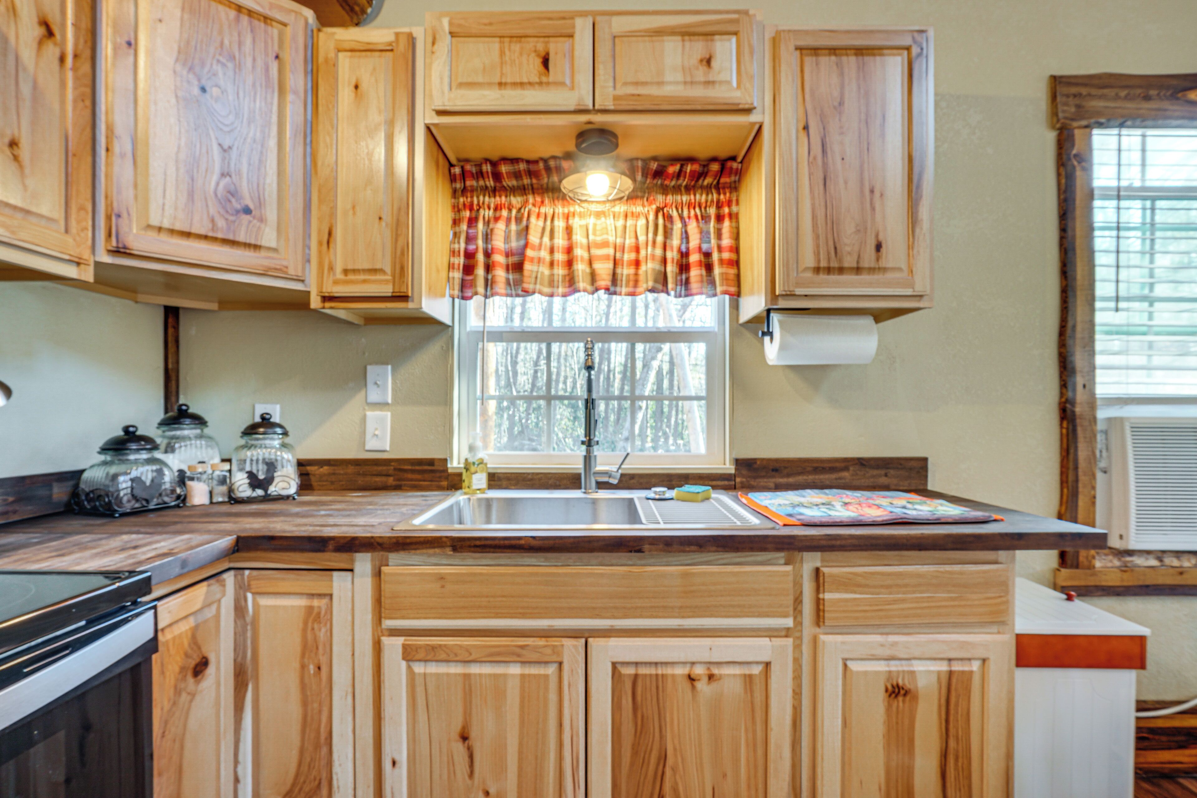 A kitchen with wooden cabinets, a window with a plaid curtain, and a built-in stove.