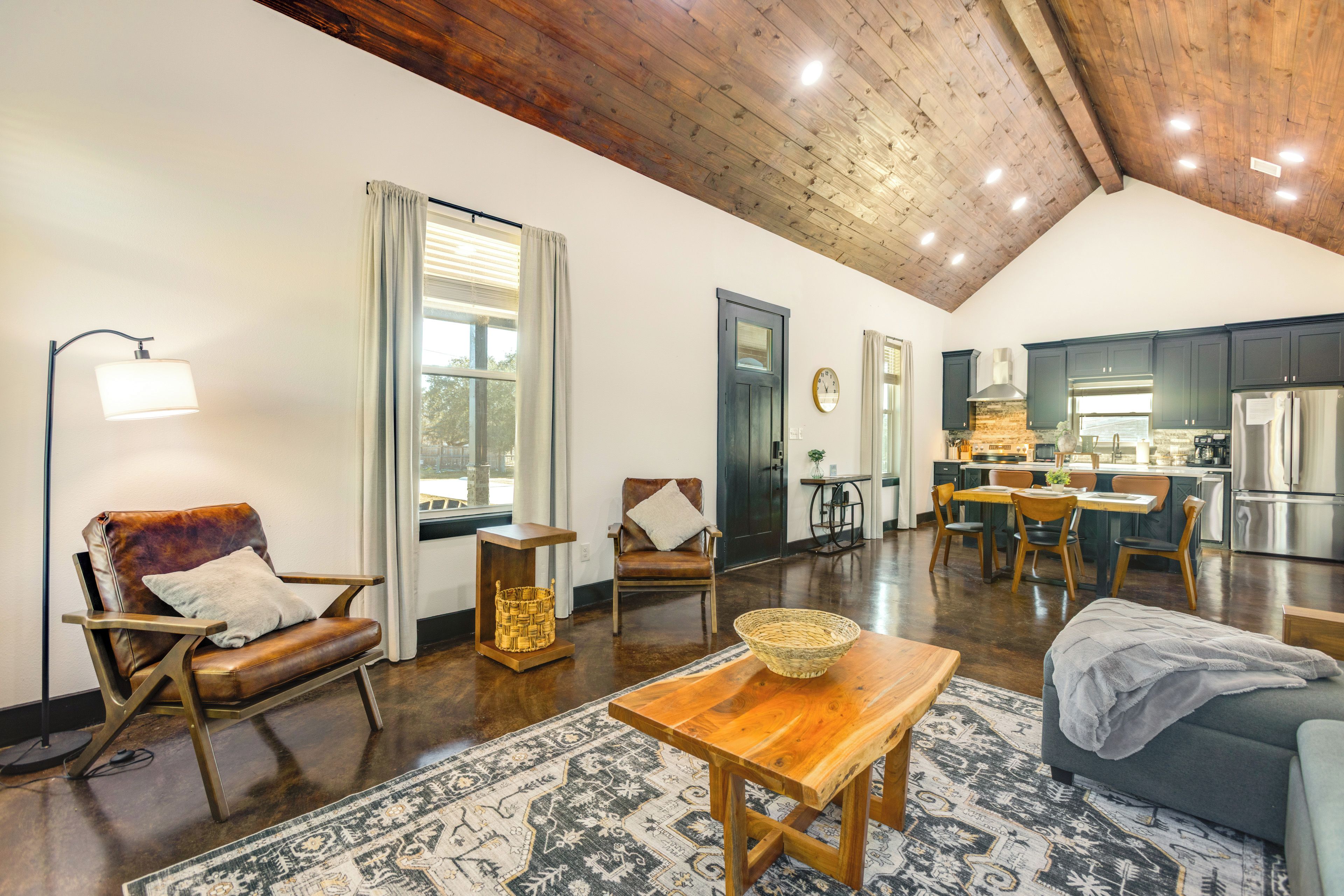 A spacious living area with a high ceiling, wooden beams, a dining table, and a kitchen in the background.