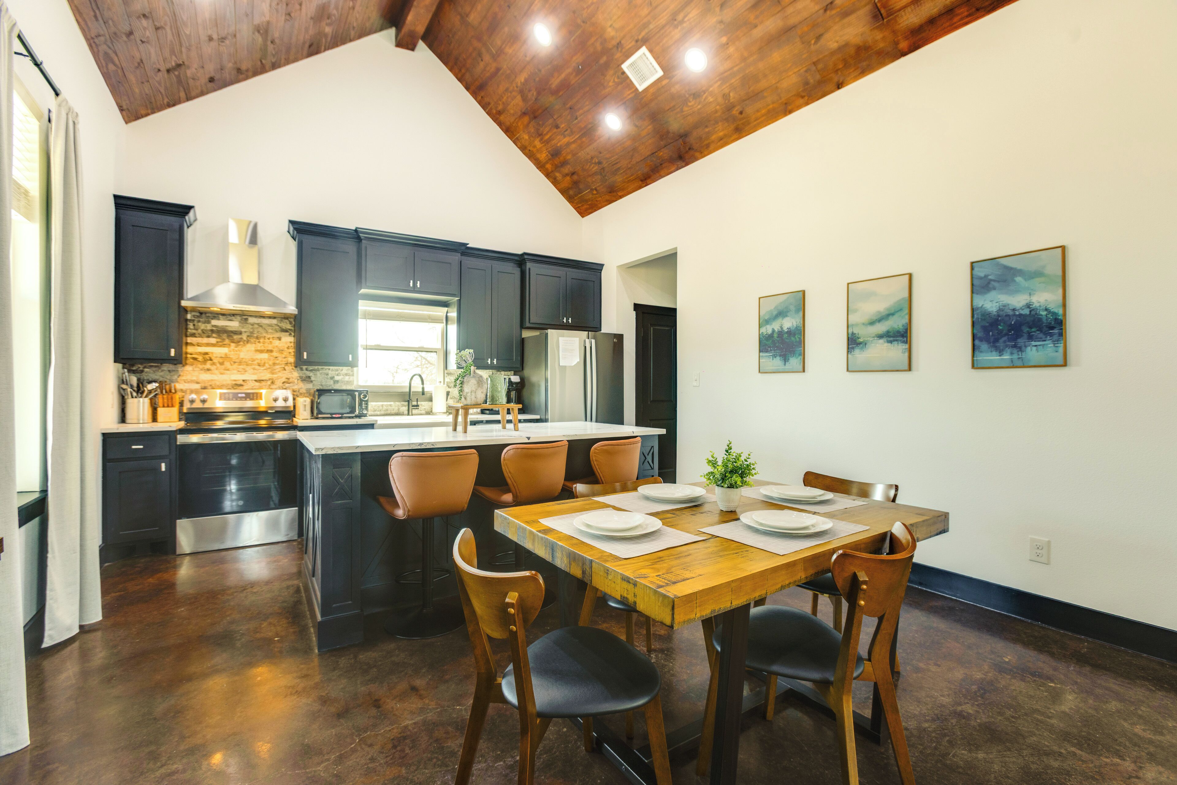 Une cuisine moderne avec des meubles de couleur sombre, des appareils en acier inoxydable et une table à manger en bois pour quatre personnes.