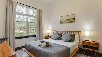 A neatly arranged bedroom with a bed, bedside tables, a window with curtains, and a painting on the wall.