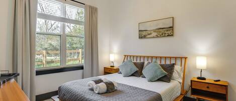 Een keurig opgemaakt slaapkamer met een bed, nachtkastjes, een raam met gordijnen en een schilderij aan de muur.