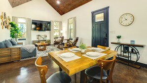 A dining area with a wooden table set for four, surrounded by chairs. A television is mounted on the wall, and a clock is visible on the wall to the right. - Modern 2BR Near Lake Somerville & Round Top (Somerville)