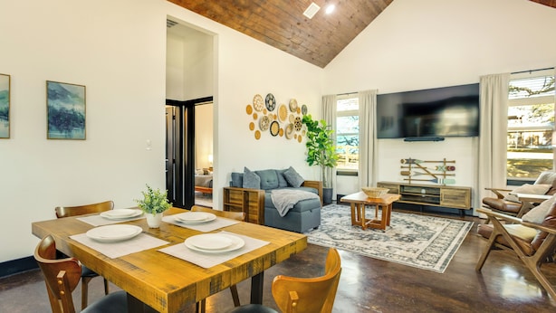 A spacious living room with a wooden dining table set for four, a comfortable sofa, a flat-screen TV, and a large window with curtains. - Modern 2BR Near Lake Somerville & Round Top (Somerville)