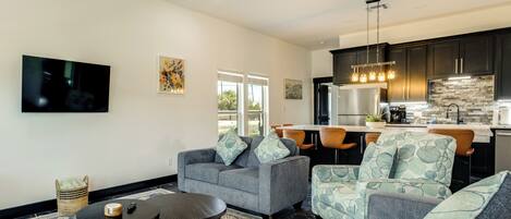 A modern living room with a sofa, armchairs, a coffee table, and a TV mounted on the wall.