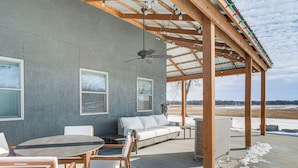An outdoor patio area with a wooden pergola, a ceiling fan, and a seating arrangement including a sofa and chairs.