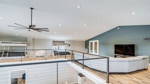 A spacious loft bedroom with a mezzanine level, a large bed, a ceiling fan, and a view of the city.