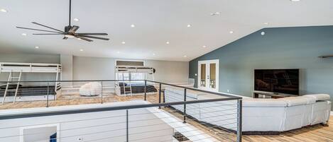 A spacious loft bedroom with a mezzanine level, a large bed, a ceiling fan, and a view of the city.