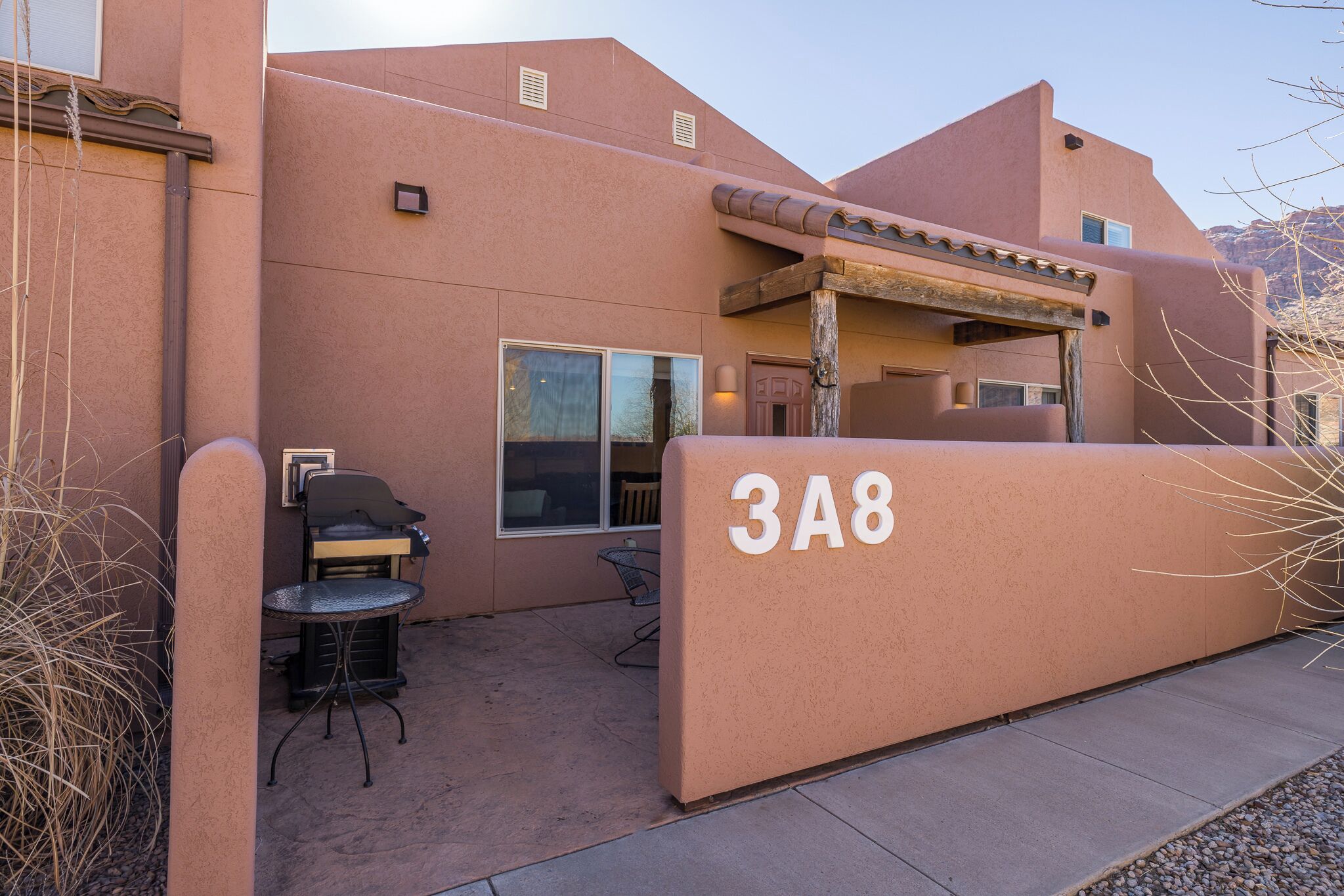 A building with a beige exterior, a barbecue area, and a patio with a table and chairs.