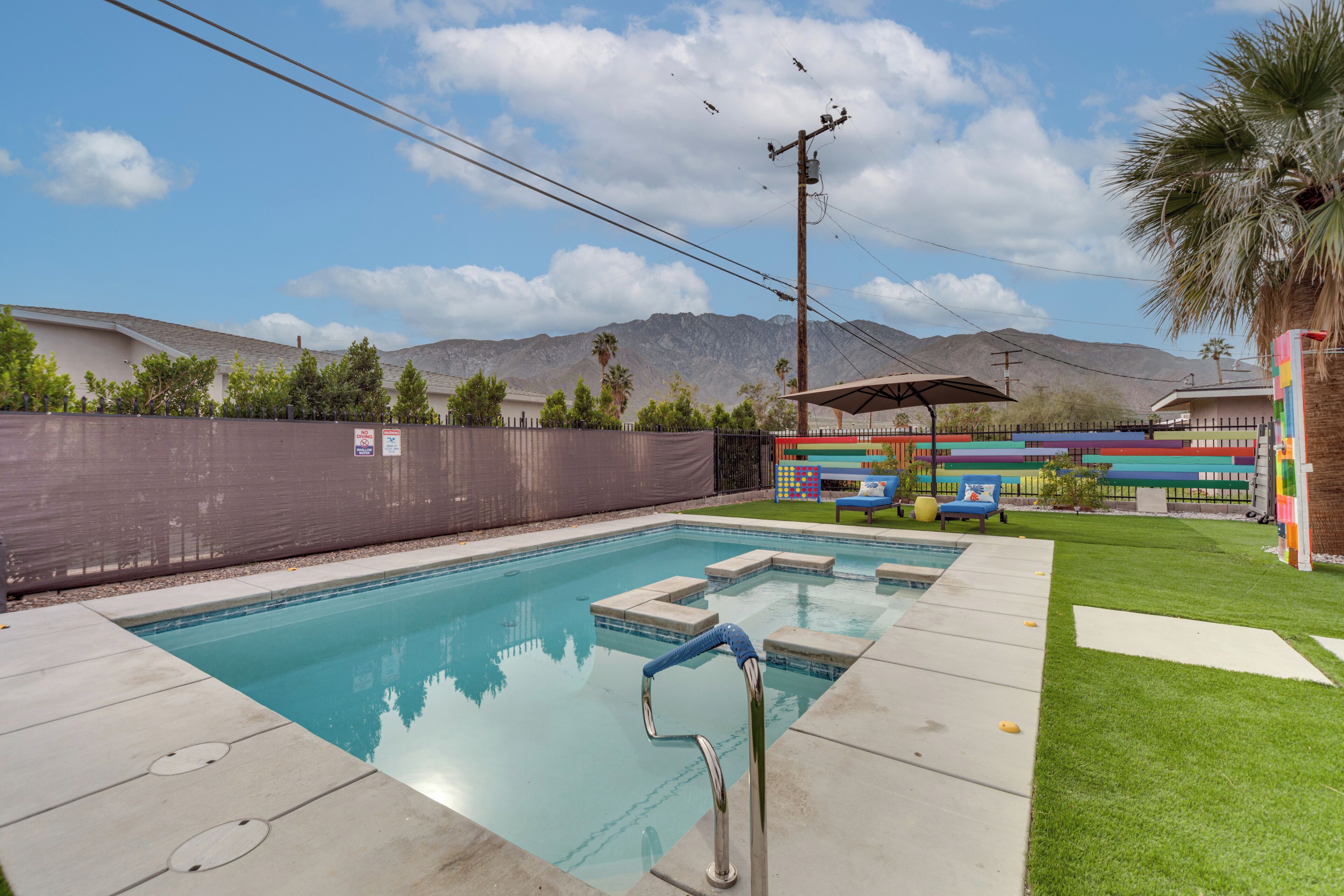 Una piscina con escalera metálica, rodeada por una zona vallada, con montañas al fondo.