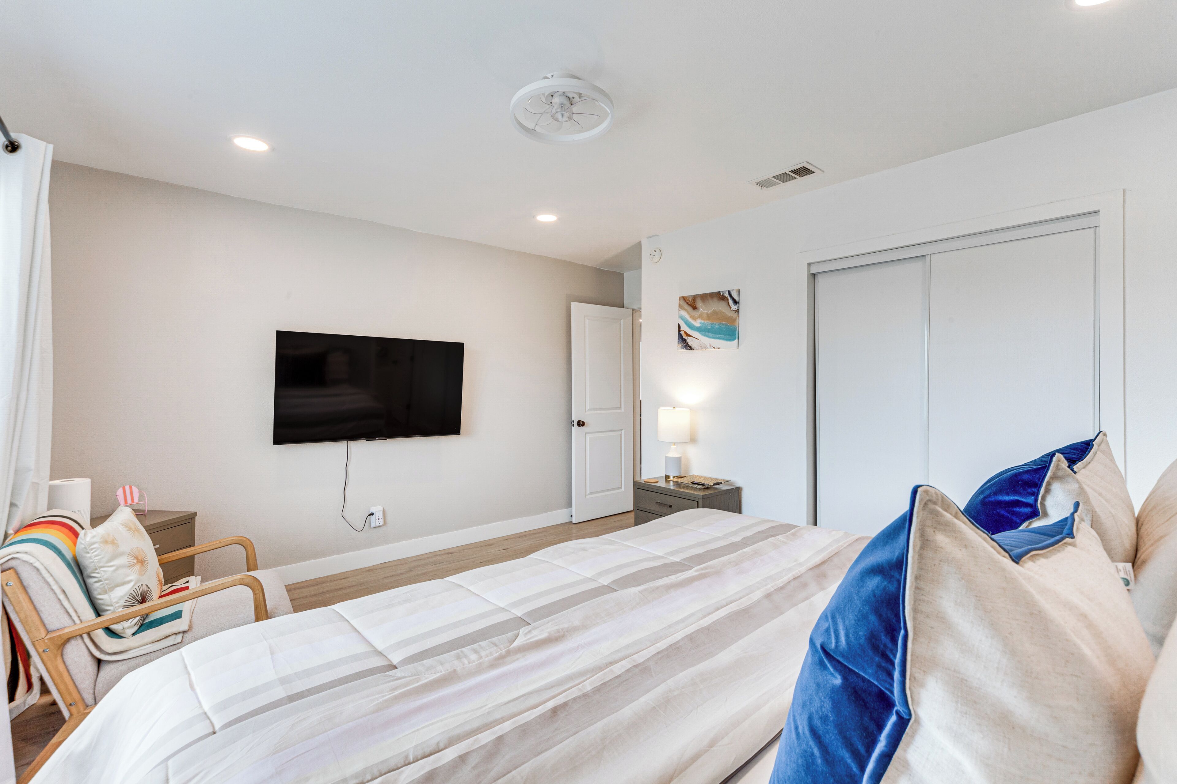 Une chambre d’hôtel avec un lit, un téléviseur fixé au mur, une table de chevet avec une lampe et une porte.