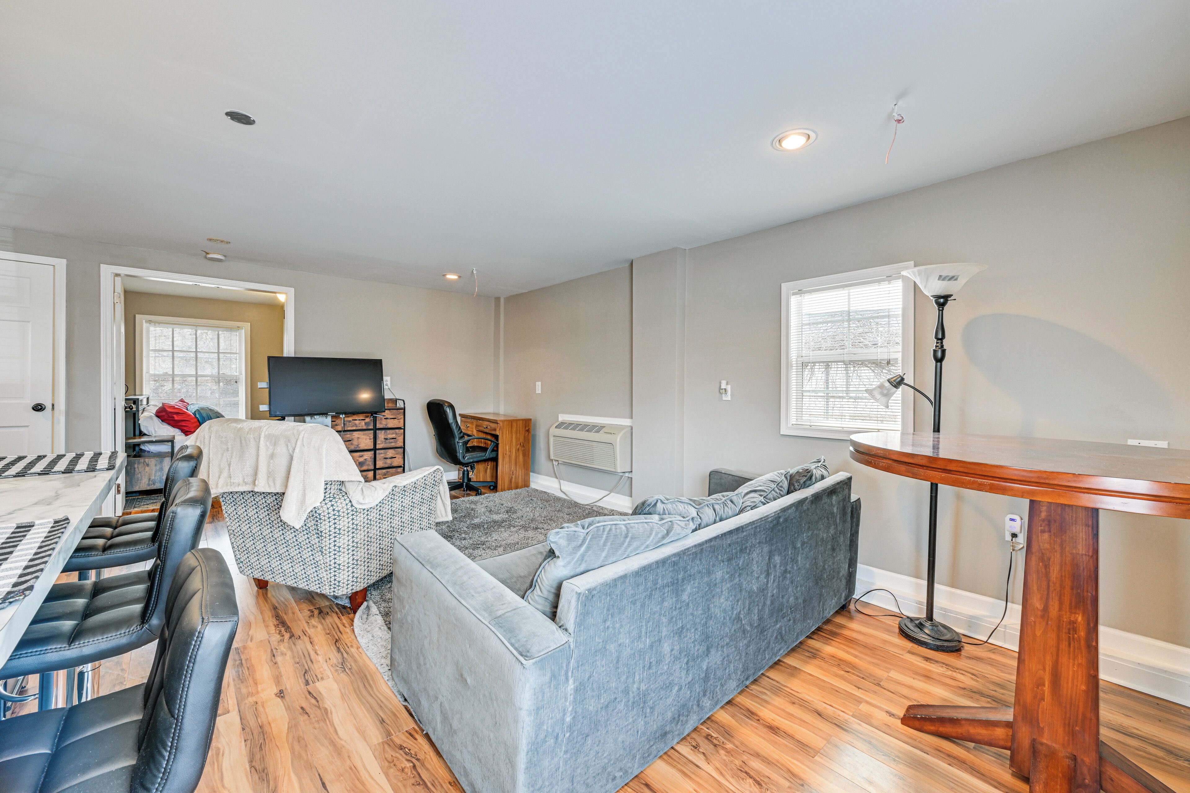 A modern living room with a grey sofa, a dining table with chairs, a TV, and a wooden floor.