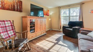 A living room with a wooden cabinet, a television, a plaid chair, a leather sofa, and a large window with curtains. - 4 Mi to Dtwn Loveland: Home w/ Hot Tub & Yard (Loveland)