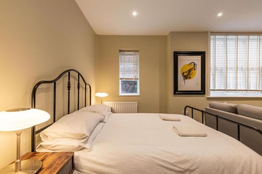 A bedroom with a bed, bedside lamp, window, radiator, and artwork.