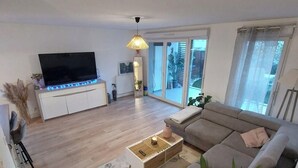 A modern living room with a flat-screen TV, a sofa, a coffee table, and a large plant.
