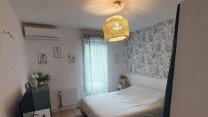 A bedroom with a bed, a dresser, a desk, a hanging lamp, and a radiator.