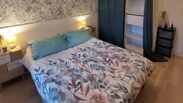 Une chambre à coucher avec une couvre-lit à motifs floraux, un luminaire suspendu, une table de chevet et une étagère.