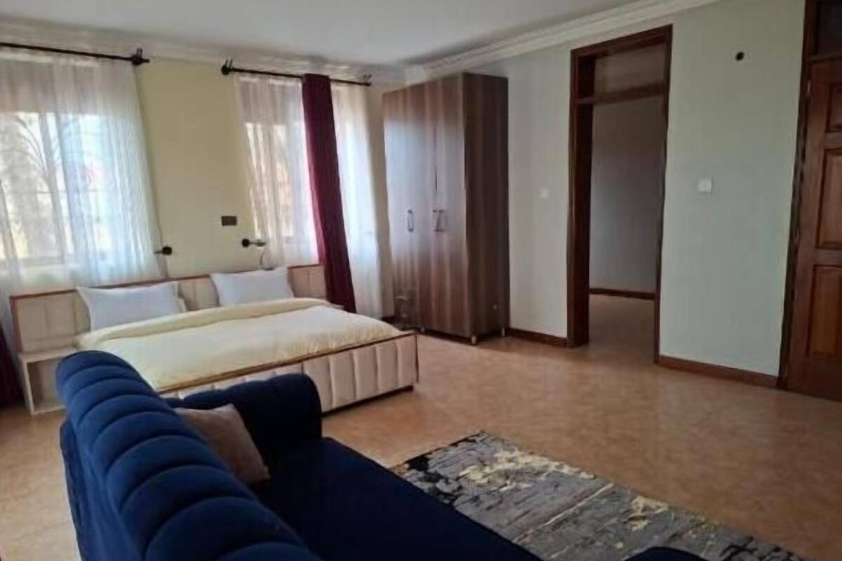 A bedroom with a bed, a blue sofa, a wooden wardrobe, and a door leading to another room.