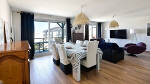 Ein modernes Wohnzimmer mit Essbereich, einer Couch, einem Fernseher und Blick nach draußen.