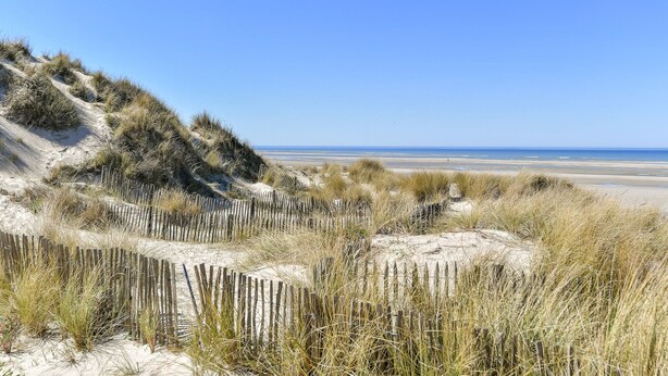 Ein sandiger Strand mit Dünen und einem Holzzaun.